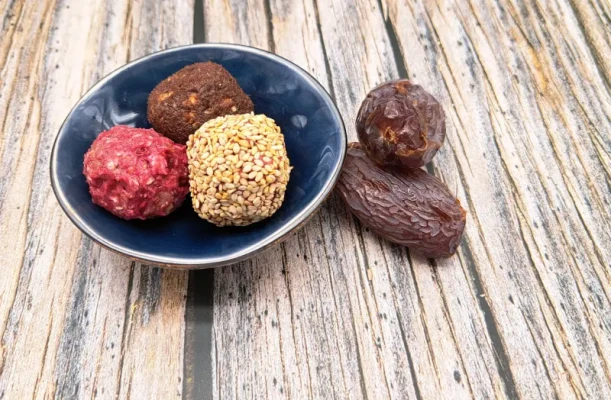 Energy Balls aus Medjool-Datteln und Haselnüssen, einige mit Kokosraspeln gewälzt, auf einem Holzbrett angerichtet