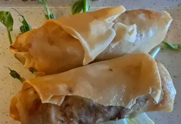 Goldbraun frittierte Thai-Frühlingsrollen, längs aufgeschnitten, mit sichtbarer Füllung aus Tofuhack, Glasnudeln, Sprossen und Gemüse
