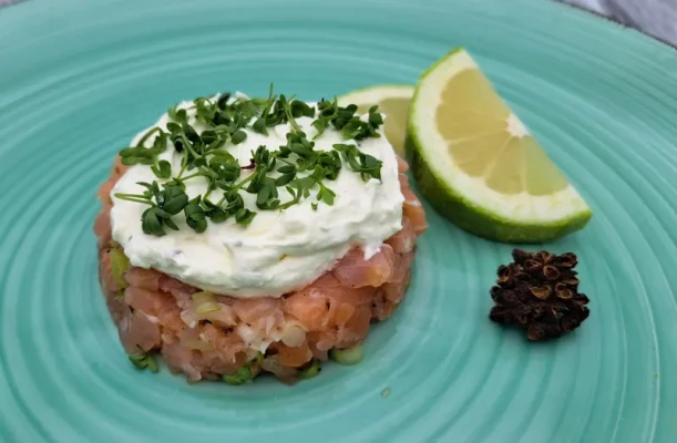 Feines Lachs-Tatar in Servierring angerichtet, gekrönt mit Limettencreme und Gartenkresse, darüber gestreuter Andalimanpfeffer