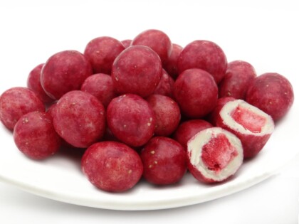 Bio Erdbeeren in Zitronenschokolade – rosa Schokokugeln auf weißem Teller, aufgeschnitten mit Erdbeerkern und weißer Schokolade